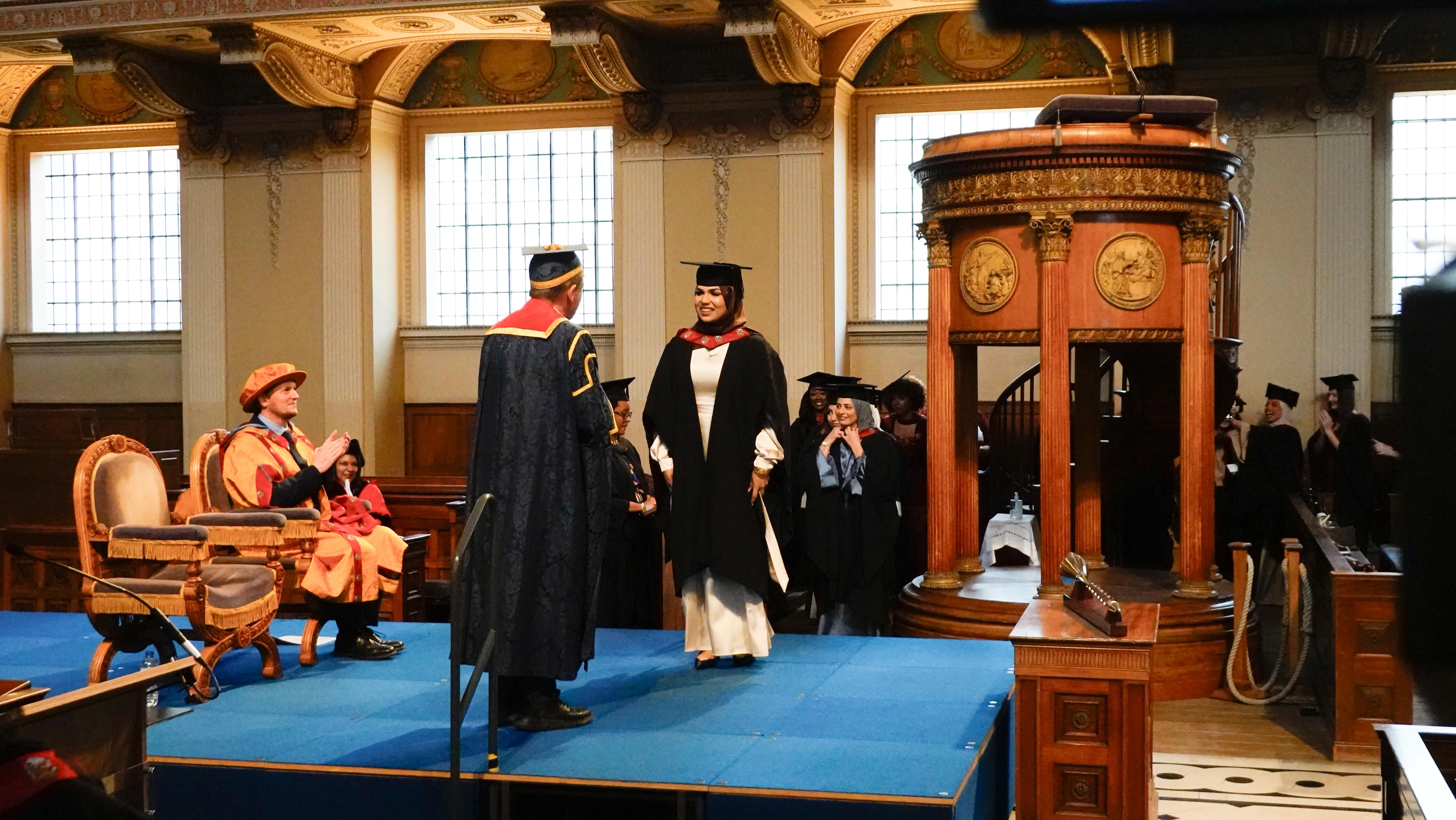 A graduate being welcomed across the stage during a ceremony